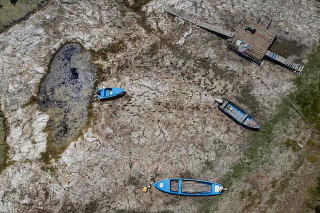 An aerial photograph taken on July 22, 2026 shows boats laying on the dried Danube river bed in front of the Calafat-Vidin bridge, connecting Bulgaria and Romania near the village Antimovo, southeastern Bulgaria. At the Romanian town of Corabia on the banks of the Danube river, some boats are stranded in shallow water full of algae in the touristic port, which lies deserted as ships can no longer dock due to sandbars (Photo by Nikolay DOYCHINOV / AFP)