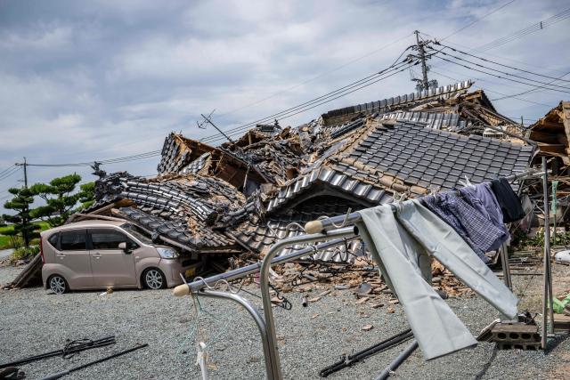 TOPSHOT - A house is seen collapsed onto a car in Hikawa, Kumamoto Prefecture on July 30, 2026 after an earthquake struck the area. The Aeon shopping mall in Kumamoto had only reopened in June, gleaming, stronger and safer thanks to the latest renovations following earthquakes in 2016, promising a place where generations could "share smiles". But despite extensive reinforcement works on the facility that suffered severe damage a decade ago, a blast triggered by a fresh quake on July 28, in the southwestern Japanese region has left it in ruins. (Photo by Yuichi YAMAZAKI / AFP)