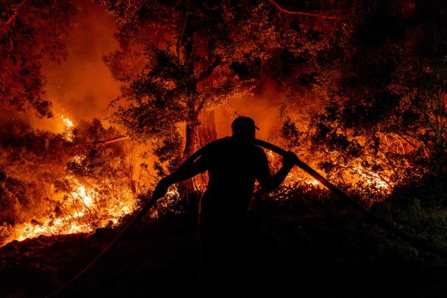 A firefighter uses a waterhose as they operate to battle a wildfire at Seydikemer district in Mugla on July 29, 2026. Turkish firefighters on July 29, 2026, battled wildfires near the country's southern tourist beaches that have forced the evacuation of hundreds of people, authorities said. Hundreds of firefighters went up against the biggest fire in Mugla province, with more than 20 planes and helicopters bombing water on the flames, the agriculture ministry said. (Photo by Murat Kocabas / AFP)
