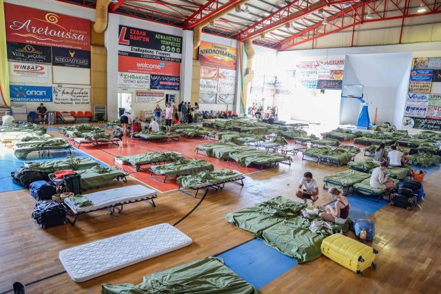 Tourists and local residents from the resort village of Agia Galini gather in an indoor stadium where they are temporarily accommodated during a wildfire in Rethymno area, in the southwest of the Greek island of Crete on July 30, 2026. Thousands of people were evacuated late on July 29, 2026, as fires threatened a tourist resort on the Greek island of Crete and continued to rage on Thursday, fanned by violent winds, a local official said. The evacuations were decided as the fire, which broke out Wednesday and had earlier killed two firefighters, got to within a kilometre of the village before changing direction in the evening. (Photo by Costas METAXAKIS / AFP)