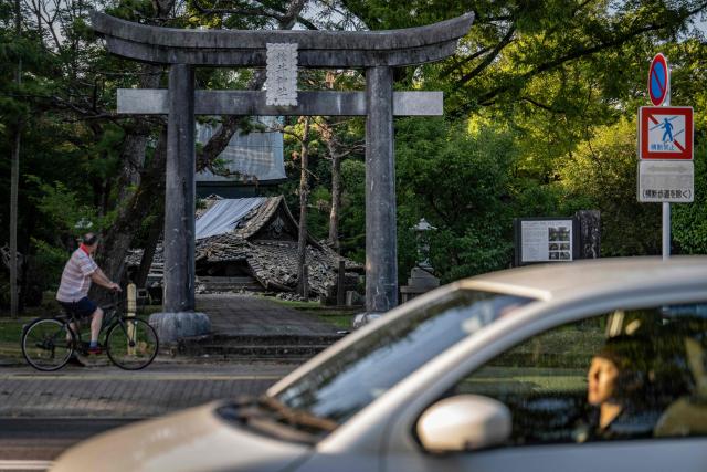 A man on a bicycle (L) stops to look at a shrine that collapsed in Yatsushiro, Kumamoto prefecture on July 30, 2026, following the July 28 earthquake. (Photo by Yuichi YAMAZAKI / AFP)