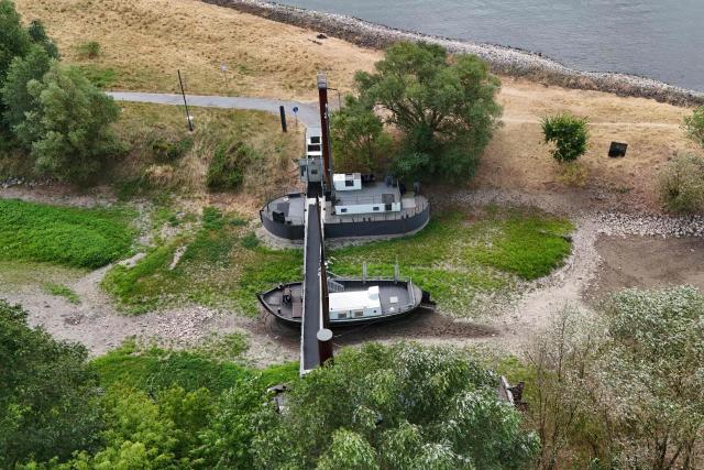 An aerial view shows three former vessels standing on dry land, including a sailing ship and an eel-fishing boat, connected by a bridge now serving as a café for day-trippers, at the old confluence of the River Wupper and the River Rhine near Leverkusen, western Germany on July 30, 2026, following exceptionally hot weather. The ship bridge at the confluence of the Wupper and the Rhine is a historic ship bridge consisting of three ships named "Unity, justice and freedom" (Einigkeit, Recht and Freiheit), which are connected by a gangway. (Photo by Ina FASSBENDER / AFP)