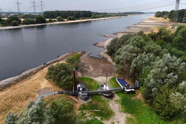 An aerial view shows three former vessels standing on dry land, including a sailing ship and an eel-fishing boat, connected by a bridge now serving as a café for day-trippers, at the old confluence of the River Wupper and the River Rhine near Leverkusen, western Germany on July 30, 2026, following exceptionally hot weather. The ship bridge at the confluence of the Wupper and the Rhine is a historic ship bridge consisting of three ships named "Unity, justice and freedom" (Einigkeit, Recht and Freiheit), which are connected by a gangway. (Photo by Ina FASSBENDER / AFP)