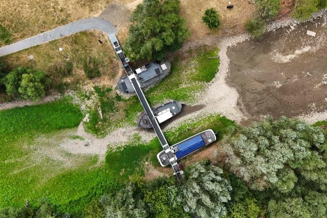 An aerial view shows three former vessels standing on dry land, including a sailing ship and an eel-fishing boat, connected by a bridge now serving as a café for day-trippers, at the old confluence of the River Wupper and the River Rhine near Leverkusen, western Germany on July 30, 2026, following exceptionally hot weather. The ship bridge at the confluence of the Wupper and the Rhine is a historic ship bridge consisting of three ships named "Unity, justice and freedom" (Einigkeit, Recht and Freiheit), which are connected by a gangway. (Photo by Ina FASSBENDER / AFP)