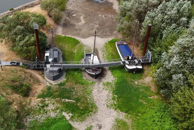 An aerial view shows three former vessels standing on dry land, including a sailing ship and an eel-fishing boat, connected by a bridge now serving as a café for day-trippers, at the old confluence of the River Wupper and the River Rhine near Leverkusen, western Germany on July 30, 2026, following exceptionally hot weather. The ship bridge at the confluence of the Wupper and the Rhine is a historic ship bridge consisting of three ships named "Unity, justice and freedom" (Einigkeit, Recht and Freiheit), which are connected by a gangway. (Photo by Ina FASSBENDER / AFP)