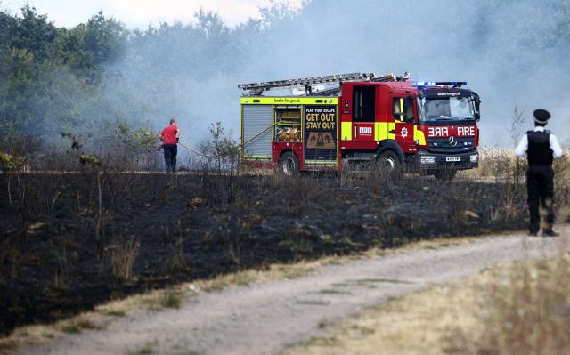 A Police officer watches as a firefighter works at the site of a wildfire in Hornchurch, east of London, on July 30, 2026. (Photo by Henry NICHOLLS / AFP)