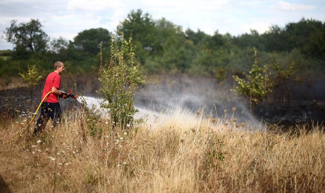 Firefighters spray water over the burnt ground at the site of a wildfire in Hornchurch, east of London, on July 30, 2026. (Photo by Henry NICHOLLS / AFP)