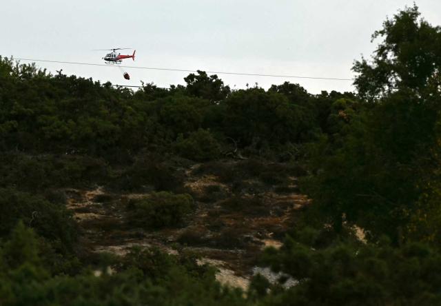 A helicopter carries a water bucket over the site of a wildfire at Dunwich Heath in eastern England on July 30, 2026. Firefighters are continuing to battle a blaze in Suffolk on July 30, under "difficult conditions" with the fire which started the previous day, said to have ravaged around 100 hectares and forced some residents and holidaymakers to evacuate. (Photo by JUSTIN TALLIS / AFP)