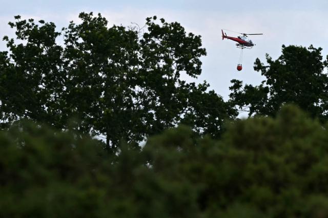 A helicopter carries a water bucket over the site of a wildfire at Dunwich Heath in eastern England on July 30, 2026. Firefighters are continuing to battle a blaze in Suffolk on July 30, under "difficult conditions" with the fire which started the previous day, said to have ravaged around 100 hectares and forced some residents and holidaymakers to evacuate. (Photo by JUSTIN TALLIS / AFP)