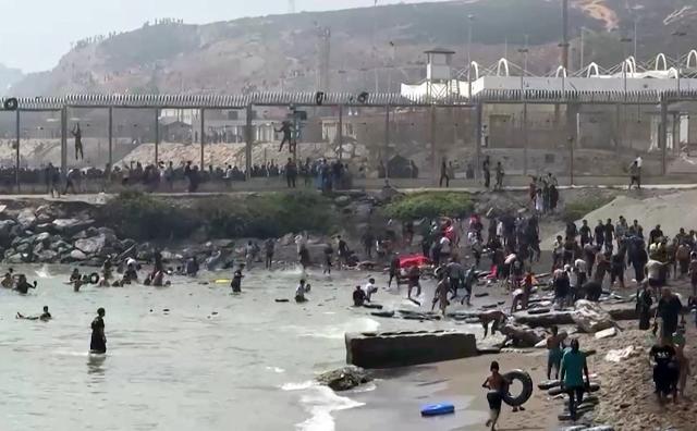 This video frame grab obtained from an AFP video shows migrants reaching the shore of Spanish north African exclave of Ceuta, after swimming around the border fence between Morocco and Spain, in Ceuta on July 30, 2026. Hundreds of migrants entered the Spanish north African exclave of Ceuta today, AFP reporters saw, many of them having swum by sea around the frontier fence. Migration from Morocco into Spain's two north African territories, Ceuta and Melilla, has long been a politically sensitive issue between the two countries, as thousands cross the border at times. AFP reporters saw a stream of adults and children, most of them wet, entering the town. (Photo by Lucía DIAZ / AFP)