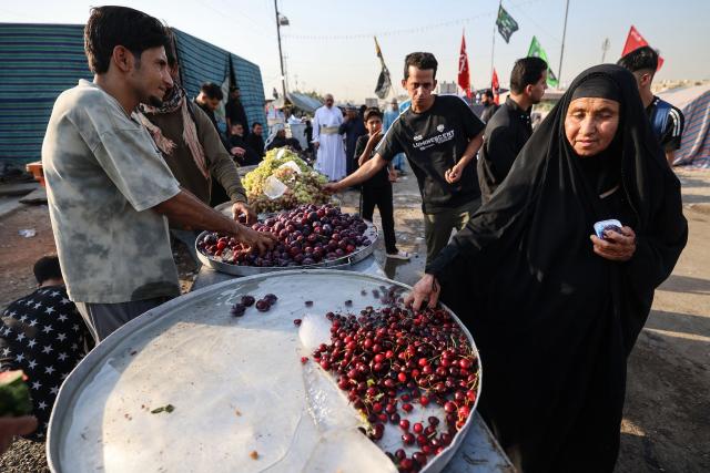 Iraqis distribute fruit to Shia pilgrims marching through Baghdad's Dora district towards Karbala to take part in the Arbaeen pilgrimage on July 30, 2026. The Arbaeen marks one of the most significant events in the Shia Muslim calendar, during which pilgrims, many from Iran, flock to Iraq to visit the holy shrines. (Photo by AHMAD AL-RUBAYE / AFP)