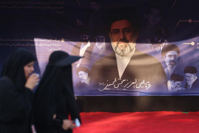 Women walk past a banner depicting Iranian supreme leader Mojtaba Khamenei as Shia pilgrims march through Baghdad's Dora district towards Karbala to take part in the Arbaeen pilgrimage on July 30, 2026. The Arbaeen marks one of the most significant events in the Shia Muslim calendar, during which pilgrims, many from Iran, flock to Iraq to visit the holy shrines. (Photo by AHMAD AL-RUBAYE / AFP)