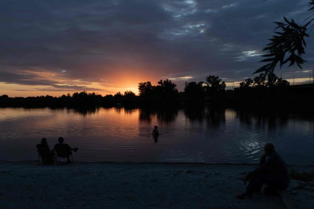 A person swims in a river at sunset during an air raid alert outside the city of Dnipro on July 30, 2026, amid the Russian invasion of Ukraine. (Photo by Roman PILIPEY / AFP)