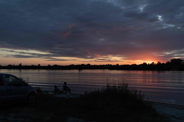 People fish in a river at sunset during an air raid alert outside the city of Dnipro on July 30, 2026, amid the Russian invasion of Ukraine. (Photo by Roman PILIPEY / AFP)