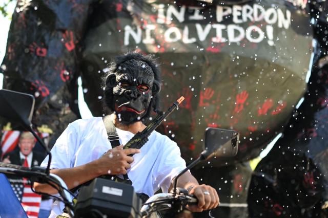 A demonstrator wearing a gorilla mask and carrying a toy rifle takes part in a march marking the 51st anniversary of the 1975 Salvadoran student massacre in San Salvador on July 30, 2026. On July 30, 1975, a protest march against the military occupation of a campus of the state-run University of El Salvador (UES) was dispersed by police using armored vehicles and gunfire during the administration of late Colonel Arturo Armando Molina (1972-1977), with university authorities reporting that around 50 students were killed and dozens disappeared. (Photo by Marvin RECINOS / AFP)
