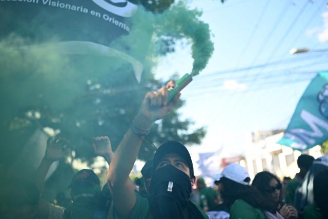 Demonstrators light green smoke flares during a march marking the 51st anniversary of the 1975 Salvadoran student massacre in San Salvador on July 30, 2026. On July 30, 1975, a protest march against the military occupation of a campus of the state-run University of El Salvador (UES) was dispersed by police using armored vehicles and gunfire during the administration of late Colonel Arturo Armando Molina (1972-1977), with university authorities reporting that around 50 students were killed and dozens disappeared. (Photo by Marvin RECINOS / AFP)