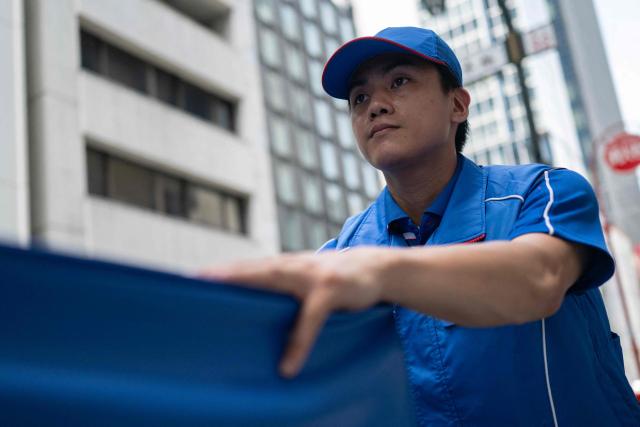 A delivery employee from Sagawa, wearing a specialised jacket with a fan to cool down, walks down a road to deliver packages in Tokyo on July 30, 2026. (Photo by Andrew CABALLERO-REYNOLDS / AFP)