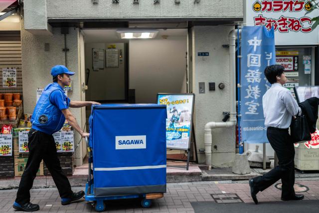 A delivery employee from Sagawa, wearing a specialised jacket with a fan to cool down, walks down a road to deliver packages in Tokyo on July 30, 2026. (Photo by Andrew CABALLERO-REYNOLDS / AFP)