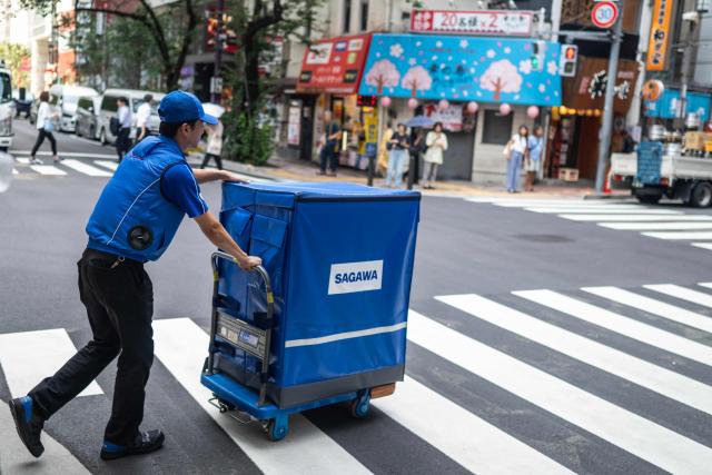 A delivery employee from Sagawa, wearing a specialised jacket with a fan to cool down, walks down a road to deliver packages in Tokyo on July 30, 2026. (Photo by Andrew CABALLERO-REYNOLDS / AFP)