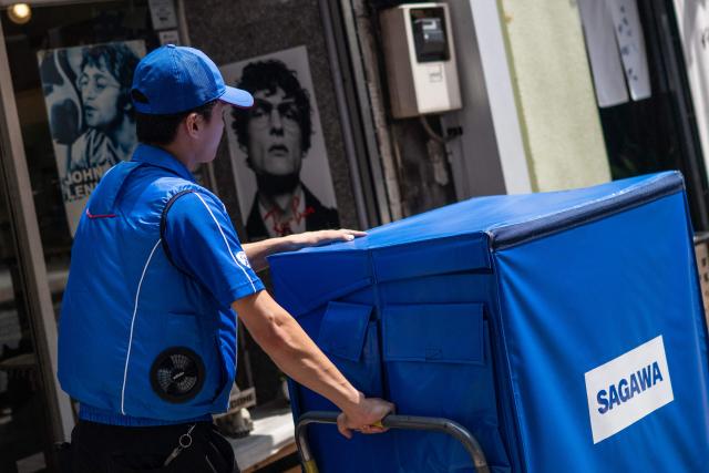 A delivery employee from Sagawa, wearing a specialised jacket with a fan to cool down, walks down a road to deliver packages in Tokyo on July 30, 2026. (Photo by Andrew CABALLERO-REYNOLDS / AFP)