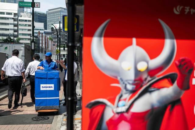 A delivery employee from Sagawa, wearing a specialised jacket with a fan to cool down, walks down a road to deliver packages in Tokyo on July 30, 2026. (Photo by Andrew CABALLERO-REYNOLDS / AFP)