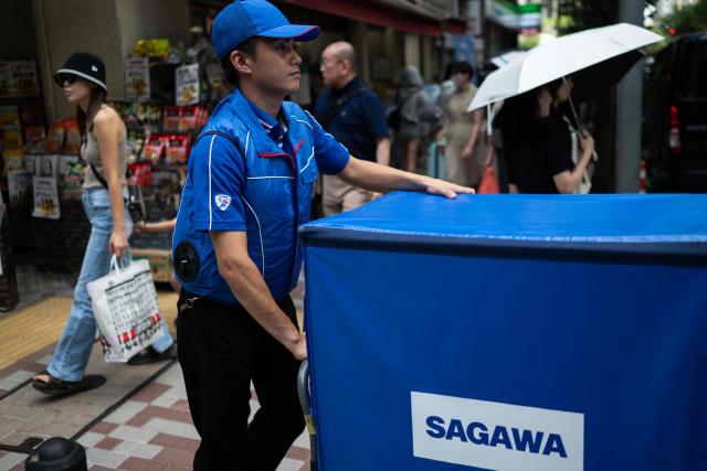A delivery employee from Sagawa, wearing a specialised jacket with a fan to cool down, walks down a road to deliver packages in Tokyo on July 30, 2026. (Photo by Andrew CABALLERO-REYNOLDS / AFP)