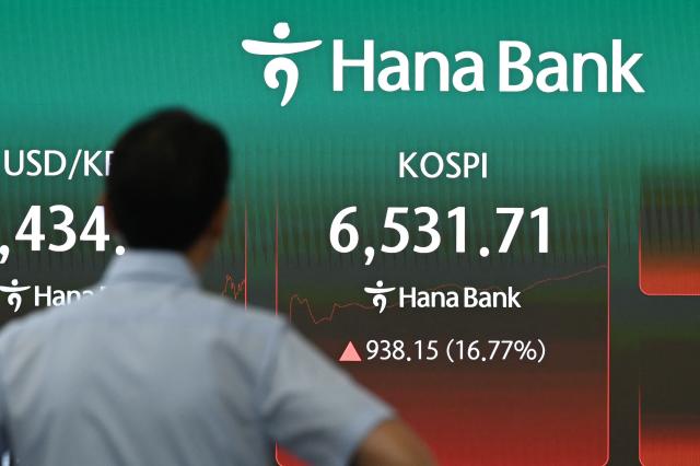 A dealer works near an electronic screen showing South Korea's benchmark stock index (KOSPI) in a foreign exchange dealing room at the Hana Bank headquarters in Seoul on July 31, 2026. South Korean stocks jumped 13 percent at open on July 31 with tentpole AI chipmaker SK hynix surging 20 percent, rebounding after a week of bruising losses. (Photo by GREG BAKER / AFP)
