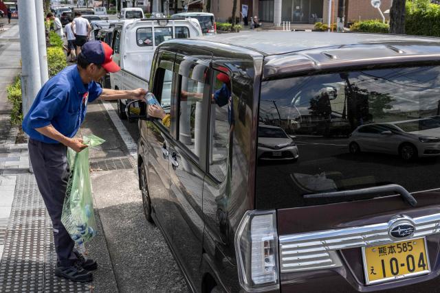 A gas station employee distributes drinks to drivers waiting in line for fuel following the the July 28 earthquake, in Yatsushiro, Kumamoto prefecture on 31 July 2026. (Photo by Yuichi YAMAZAKI / AFP)