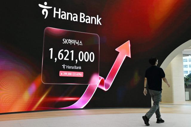 A man walks past an electronic screen showing the SK Hynix stock price outside a foreign exchange dealing room at the Hana Bank headquarters in Seoul on July 31, 2026. South Korean stocks jumped 13 percent at open on July 31 with tentpole AI chipmaker SK hynix surging 20 percent, rebounding after a week of bruising losses. (Photo by GREG BAKER / AFP)