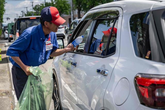 A gas station employee distributes drinks to drivers waiting in line for fuel following the the July 28 earthquake, in Yatsushiro, Kumamoto prefecture on 31 July 2026. (Photo by Yuichi YAMAZAKI / AFP)