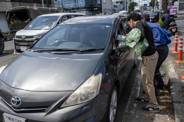Gas station employees distribute hand fan to drivers waiting in line for fuel following the the July 28 earthquake, in Yatsushiro, Kumamoto prefecture on 31 July 2026. (Photo by Yuichi YAMAZAKI / AFP)