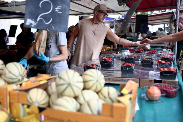 (FILES) A fruit vendor exchanges money with a customer at an open-air market in Paris on July 15, 2025. French consumer prices rose by 2.1 percent year-on-year in July, after June brought a 1.8 percent increase, driven by higher prices for services and energy, statistics body INSEE reported on July 31, 2026. (Photo by Behrouz MEHRI / AFP)
