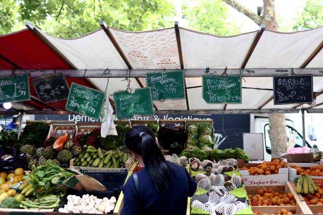 (FILES) A customer stands in front of a fruit and vegetable stall at an open-air market in Paris on July 15, 2025. French consumer prices rose by 2.1 percent year-on-year in July, after June brought a 1.8 percent increase, driven by higher prices for services and energy, statistics body INSEE reported on July 31, 2026. (Photo by Behrouz MEHRI / AFP)