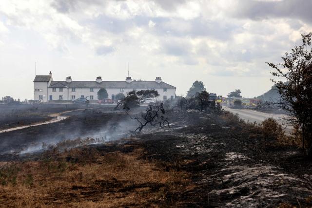 Scorched burnt-out heath land is pictured in front of Coastguard Cottages, following a wildfire, at Dunwich Heath in eastern England on July 31, 2026. Firefighters in eastern England were "making good progress" Thursday battling a "dynamic" wildfire which has engulfed swathes of heathland and prompted the evacuation of dozens of residents and visitors, local officials said. (Photo by Humphrey Nemar / POOL / AFP)