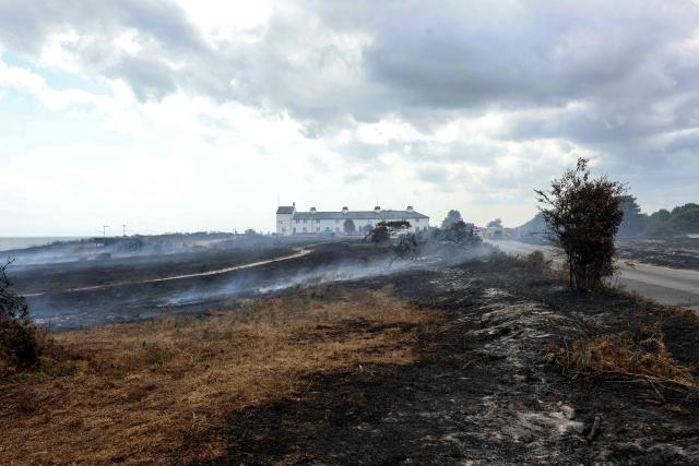 Scorched burnt-out heath land is pictured in front of Coastguard Cottages, following a wildfire, at Dunwich Heath in eastern England on July 31, 2026. Firefighters in eastern England were "making good progress" Thursday battling a "dynamic" wildfire which has engulfed swathes of heathland and prompted the evacuation of dozens of residents and visitors, local officials said. (Photo by Humphrey Nemar / POOL / AFP)