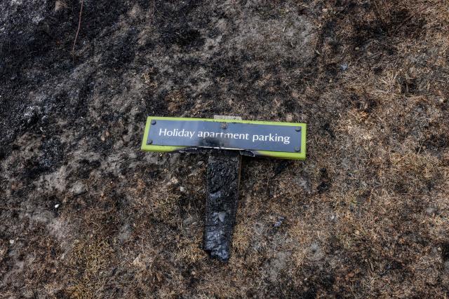 A scorched burnt-out parking sign is pictured, following a wildfire, at Dunwich Heath in eastern England on July 31, 2026. Firefighters in eastern England were "making good progress" Thursday battling a "dynamic" wildfire which has engulfed swathes of heathland and prompted the evacuation of dozens of residents and visitors, local officials said. (Photo by Humphrey Nemar / POOL / AFP)