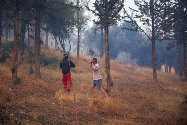 A local resident gestures as firefighters fight a wildfire in Haidari, a suburb west of Athens, on July 31, 2026. New wildfires fed by strong winds broke out in Greece on July 31, 2026 giving firefighters little respite and forcing Civil Protection officials to order the partial evacuation of part of a suburb west of Athens. (Photo by Aris Oikonomou / AFP)