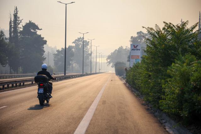 A motorcyclist rides along a smoke filled road during a wildfire in Haidari, a suburb west of Athens, on July 31, 2026. New wildfires fed by strong winds broke out in Greece on July 31, 2026 giving firefighters little respite and forcing Civil Protection officials to order the partial evacuation of part of a suburb west of Athens. (Photo by Aris Oikonomou / AFP)