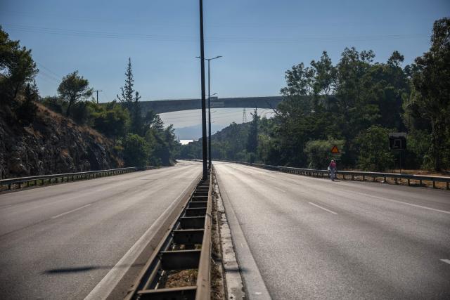 A local resident walks along an empty road during a wildfire in Haidari, a suburb west of Athens, on July 31, 2026. New wildfires fed by strong winds broke out in Greece on July 31, 2026 giving firefighters little respite and forcing Civil Protection officials to order the partial evacuation of part of a suburb west of Athens. (Photo by Aris Oikonomou / AFP)