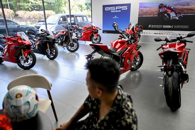 This picture taken on July 21, 2026 shows a man looking at motorcycles in a showroom of a store in Chongqing, southwestern China. The roar of engines fills the night air in China's Chongqing city as tourists awkwardly clamber onto gleaming motorbikes and cling to muscular drivers to star in personalised videos. Chongqing has been an industry hub since 1979, when state-owned military equipment manufacturer Jialing began producing civilian motorcycles in the city. Motorbikes quickly became popular, and the city now accounts for more than a third of China's total motorbike production. (Photo by WANG Zhao / AFP) / To go with 'CHINA-MOTORBIKE-INTERNET,FOCUS' by Sam DAVIES