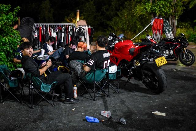 This picture taken on July 21, 2026 shows a group of riders waiting for customers for riding photo and video services along a street in Chongqing, southwestern China. The roar of engines fills the night air in China's Chongqing city as tourists awkwardly clamber onto gleaming motorbikes and cling to muscular drivers to star in personalised videos. (Photo by WANG Zhao / AFP) / To go with 'CHINA-MOTORBIKE-INTERNET,FOCUS' by Sam DAVIES