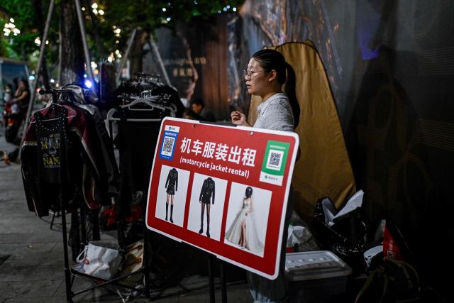 This picture taken on July 21, 2026 shows a motorcycle jacket rental business owner waiting on customers for a riding photo and video service in Chongqing, southwestern China. The roar of engines fills the night air in China's Chongqing city as tourists awkwardly clamber onto gleaming motorbikes and cling to muscular drivers to star in personalised videos. (Photo by WANG Zhao / AFP) / To go with 'CHINA-MOTORBIKE-INTERNET,FOCUS' by Sam DAVIES