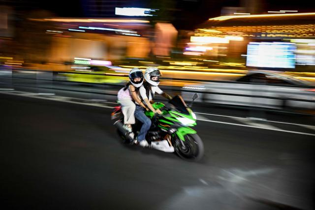 This picture taken on July 21, 2026 shows two women riding a motorcycle along a street in Chongqing, southwestern China. The roar of engines fills the night air in China's Chongqing city as tourists awkwardly clamber onto gleaming motorbikes and cling to muscular drivers to star in personalised videos. (Photo by WANG Zhao / AFP) / To go with 'CHINA-MOTORBIKE-INTERNET,FOCUS' by Sam DAVIES
