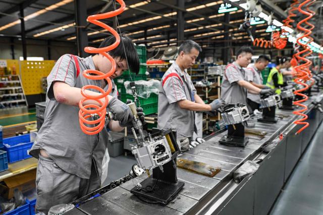 This picture taken on July 21, 2026 shows workers assembling engines for motorcycles at the Shineray factory in Chongqing, southwestern China. The roar of engines fills the night air in China's Chongqing city as tourists awkwardly clamber onto gleaming motorbikes and cling to muscular drivers to star in personalised videos. Chongqing has been an industry hub since 1979, when state-owned military equipment manufacturer Jialing began producing civilian motorcycles in the city. Motorbikes quickly became popular, and the city now accounts for more than a third of China's total motorbike production. (Photo by WANG Zhao / AFP) / To go with 'CHINA-MOTORBIKE-INTERNET,FOCUS' by Sam DAVIES