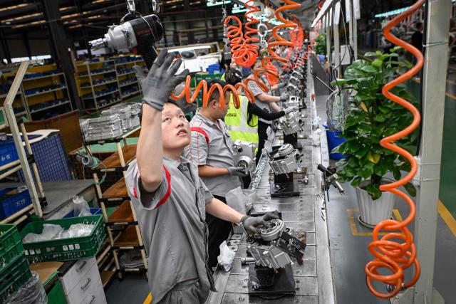 This picture taken on July 21, 2026 shows workers assembling engines for motorcycles at the Shineray factory in Chongqing, southwestern China. The roar of engines fills the night air in China's Chongqing city as tourists awkwardly clamber onto gleaming motorbikes and cling to muscular drivers to star in personalised videos. Chongqing has been an industry hub since 1979, when state-owned military equipment manufacturer Jialing began producing civilian motorcycles in the city. Motorbikes quickly became popular, and the city now accounts for more than a third of China's total motorbike production. (Photo by WANG Zhao / AFP) / To go with 'CHINA-MOTORBIKE-INTERNET,FOCUS' by Sam DAVIES