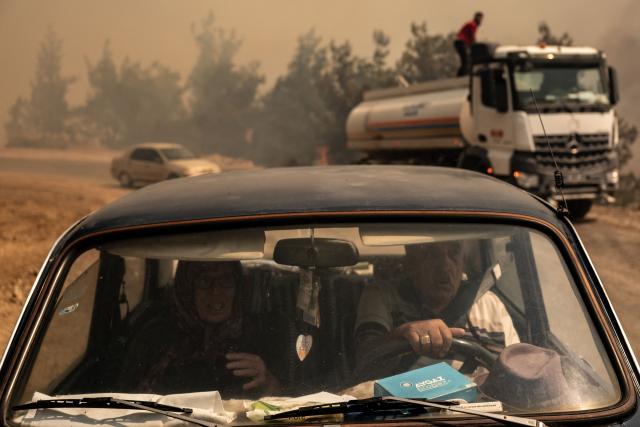 A man drives his car on a road as vegetation burns during a wildfire at Cine district in Aydin, on July 31, 2026. Hundreds of firefighters were on July 31, 2026 battling strong winds to quench a wildfire in southwestern Turkey as high winds stoked a new blaze, complicating efforts to bring the fires under control, a minister said. Although Turkey experienced early wildfires in 2025 due to drought, it had been largely spared until now thanks to heavy winter rains and snowfall that replenished groundwater and protected vegetation. (Photo by Murat Kocabas / AFP)