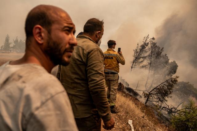 Volunteers and firefighters stay next to burning trees and vegetation during a wildfire at Cine district in Aydin, on July 31, 2026. Hundreds of firefighters were on July 31, 2026 battling strong winds to quench a wildfire in southwestern Turkey as high winds stoked a new blaze, complicating efforts to bring the fires under control, a minister said. Although Turkey experienced early wildfires in 2025 due to drought, it had been largely spared until now thanks to heavy winter rains and snowfall that replenished groundwater and protected vegetation. (Photo by Murat Kocabas / AFP)