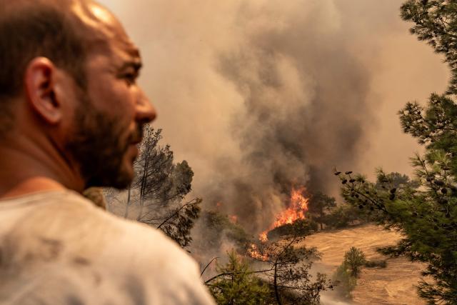A volunteer stays next to burning vegetation during a wildfire in Cine district in Aydin, on July 31, 2026. Hundreds of firefighters were on July 31, 2026 battling strong winds to quench a wildfire in southwestern Turkey as high winds stoked a new blaze, complicating efforts to bring the fires under control, a minister said. Although Turkey experienced early wildfires in 2025 due to drought, it had been largely spared until now thanks to heavy winter rains and snowfall that replenished groundwater and protected vegetation. (Photo by Murat Kocabas / AFP)