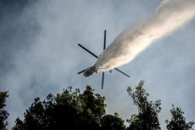 A firefighting helicopter drops water over a wildfire in the area of Porto Germeno, some 70 kilometres (45 miles) northwest of Athens in the region of Viotia, on August 2, 2026. Hundreds of firefighters in Greece battle to save a popular coastal resort northwest of Athens as violent winds continued to lash the country, hampering operations. Hit hard by the climate crisis like the rest of the Mediterranean region, the country is plagued by wildfires every summer due to high temperatures, frequent heatwaves, and drought. (Photo by Angelos TZORTZINIS / AFP)