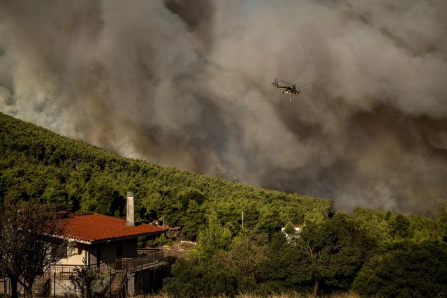 A firefighting helicopter flies as smoke rises from a wildfire in the area of Porto Germeno, some 70 kilometres (45 miles) northwest of Athens in the region of Viotia, on August 2, 2026. Hundreds of firefighters in Greece battle to save a popular coastal resort northwest of Athens as violent winds continued to lash the country, hampering operations. Hit hard by the climate crisis like the rest of the Mediterranean region, the country is plagued by wildfires every summer due to high temperatures, frequent heatwaves, and drought. (Photo by Angelos TZORTZINIS / AFP)